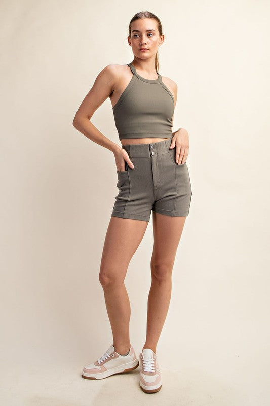 A person wearing a green ribbed crop top and high-waisted gray Cotton Stretch Twill Short Pant with button closure. The slim-fit short boasts a high-rise design, making the outfit both casual and fitted.