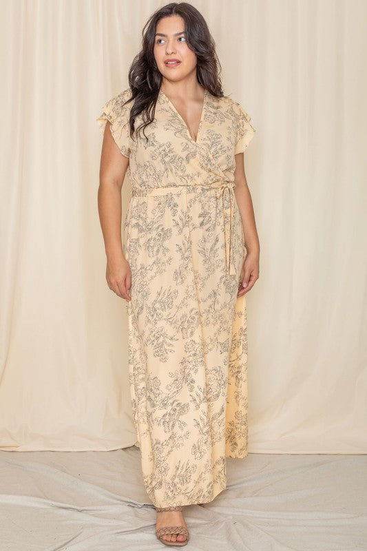 A woman wearing a Floral Surplice Sash Sundress, which is light yellow and unlined, stands smiling against a cream-colored background.