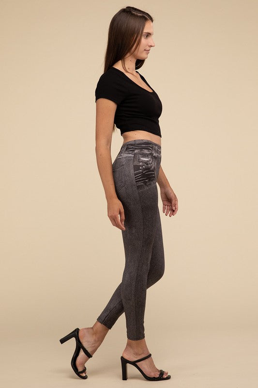 A person wearing Denim Leggings in a high-waisted black design and paired with black heels poses against a plain beige background, highlighting the sleek, stretchy fit.