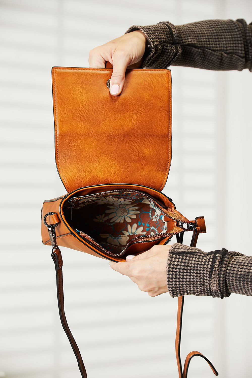 A person wearing a dark sweater and jeans holds the SHOMICO PU Leather Crossbody Bag, a stylish accessory in orange-brown featuring a flap and buckle detail.