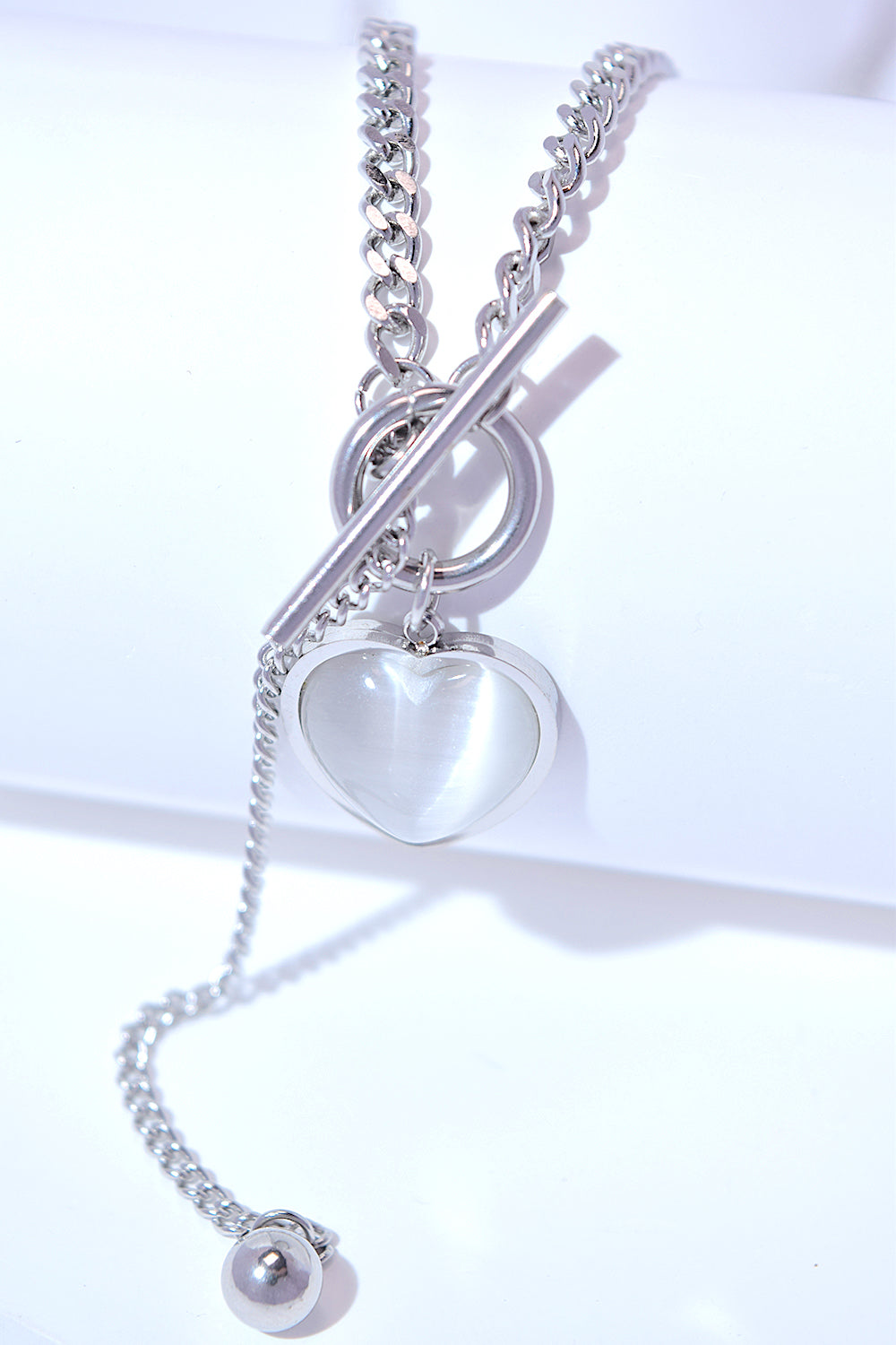 A Titanium Steel Heart Necklace with a heart-shaped pendant and a small key charm, featuring a delicate cat's eye stone, on a white background.