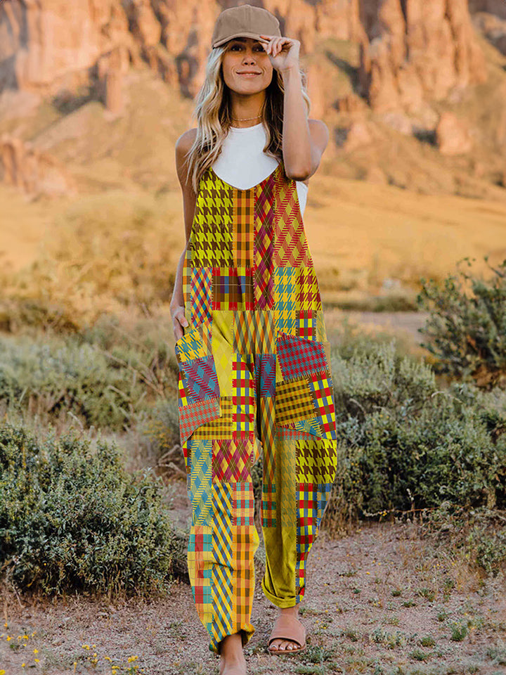 A woman stands outdoors in front of a rocky landscape, wearing the Full Size Printed V-Neck Sleeveless Jumpsuit and a brown brimmed hat. She is smiling and holding the brim of her hat with one hand, exuding the carefree vibe of this vibrant and colorful jumpsuit.