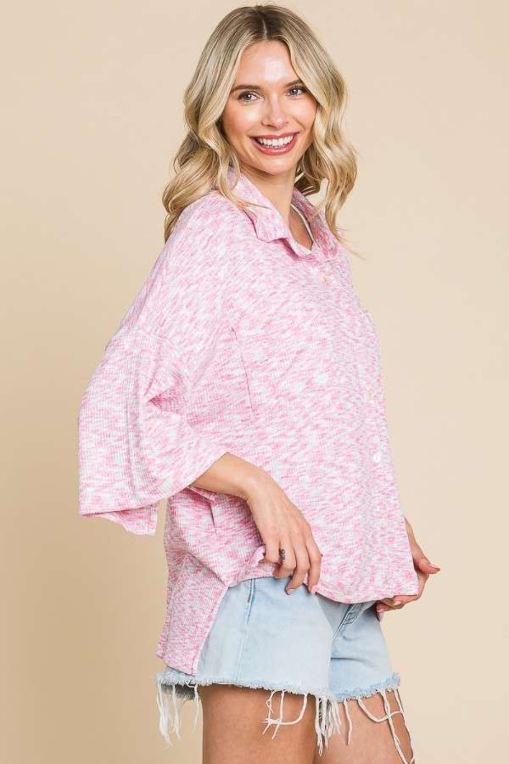 A person wearing the Culture Code Button Up Drop Shoulder Slit Shirt in pink, along with a white crop top, denim shorts, and a red cap, smiles against a neutral background.