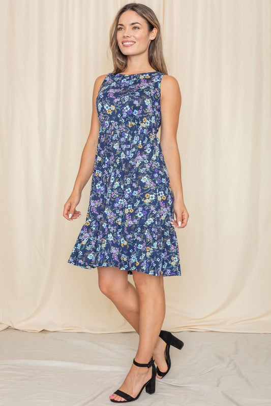 A woman in a Sleeveless Botanical Floral Tiered Dress and black sandals stands elegantly in front of a pink curtain.