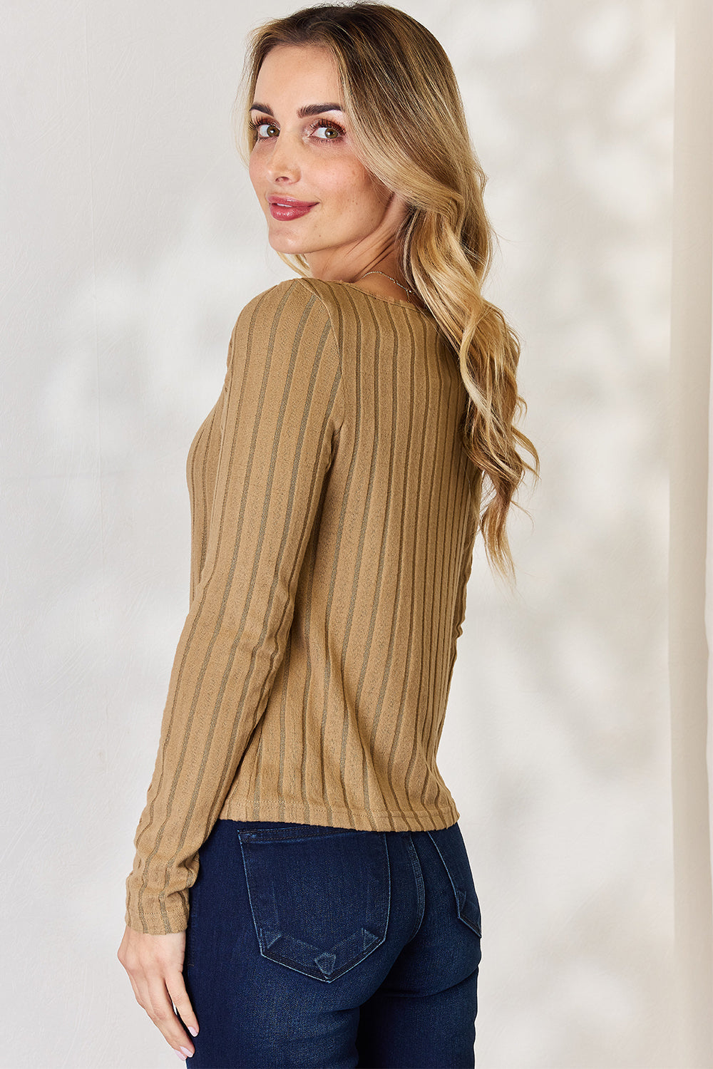 A person is standing and smiling, wearing the Basic Bae Full Size Ribbed Long Sleeve T-Shirt in light brown along with jeans. The basic style is perfect for any casual outing.