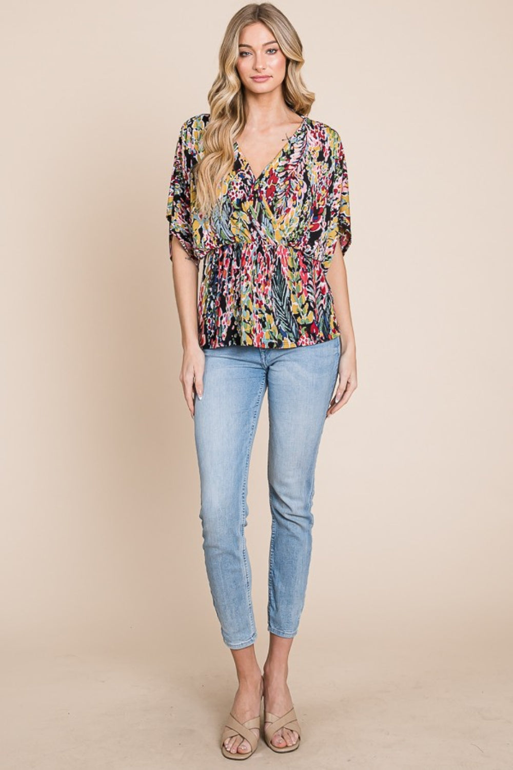 A woman wearing the BOMBOM Printed Surplice Peplum Blouse and blue jeans holds the brim of her white hat with one hand.