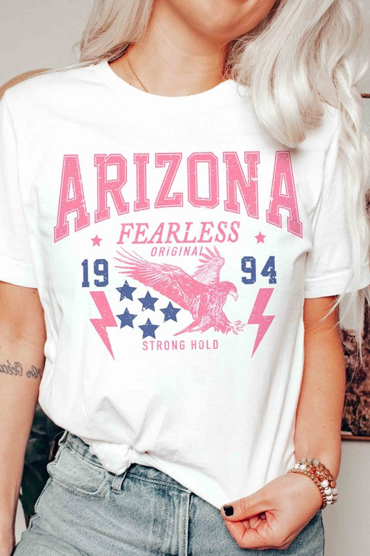 A woman with long light hair is wearing jeans and a 100% cotton ARIZONA EAGLE 1994 Graphic Tee, which features the text "ARIZONA FEARLESS ORIGINAL 1994 STRONG HOLD" along with an eagle, stars, and lightning bolts.