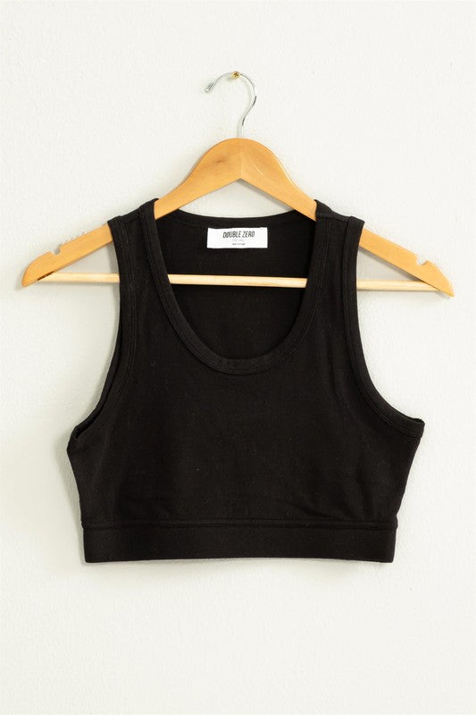 The "All I Need Cropped Tank Top," featuring a light blue hue and a fitted silhouette, hangs on a wooden hanger against a white wall.