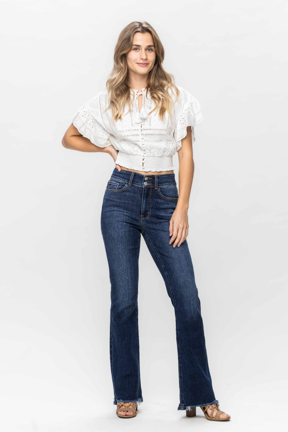 A person wearing trendy and stylish Judy Blue Full Size Frayed Hem Bootcut Jeans with a distressed finish and open-toed sandals is standing against a plain white background.