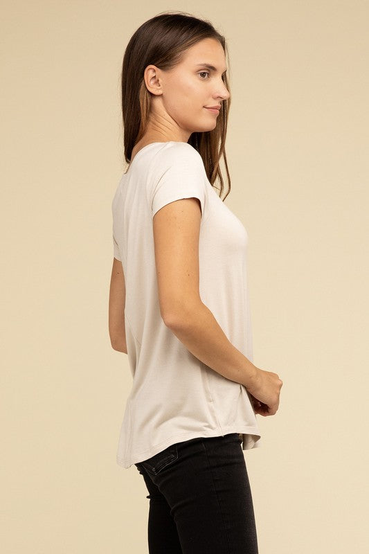 A person with long hair is wearing a blue Flowy Round Hem Rayon Short Sleeve Top and black pants, standing against a plain beige background.