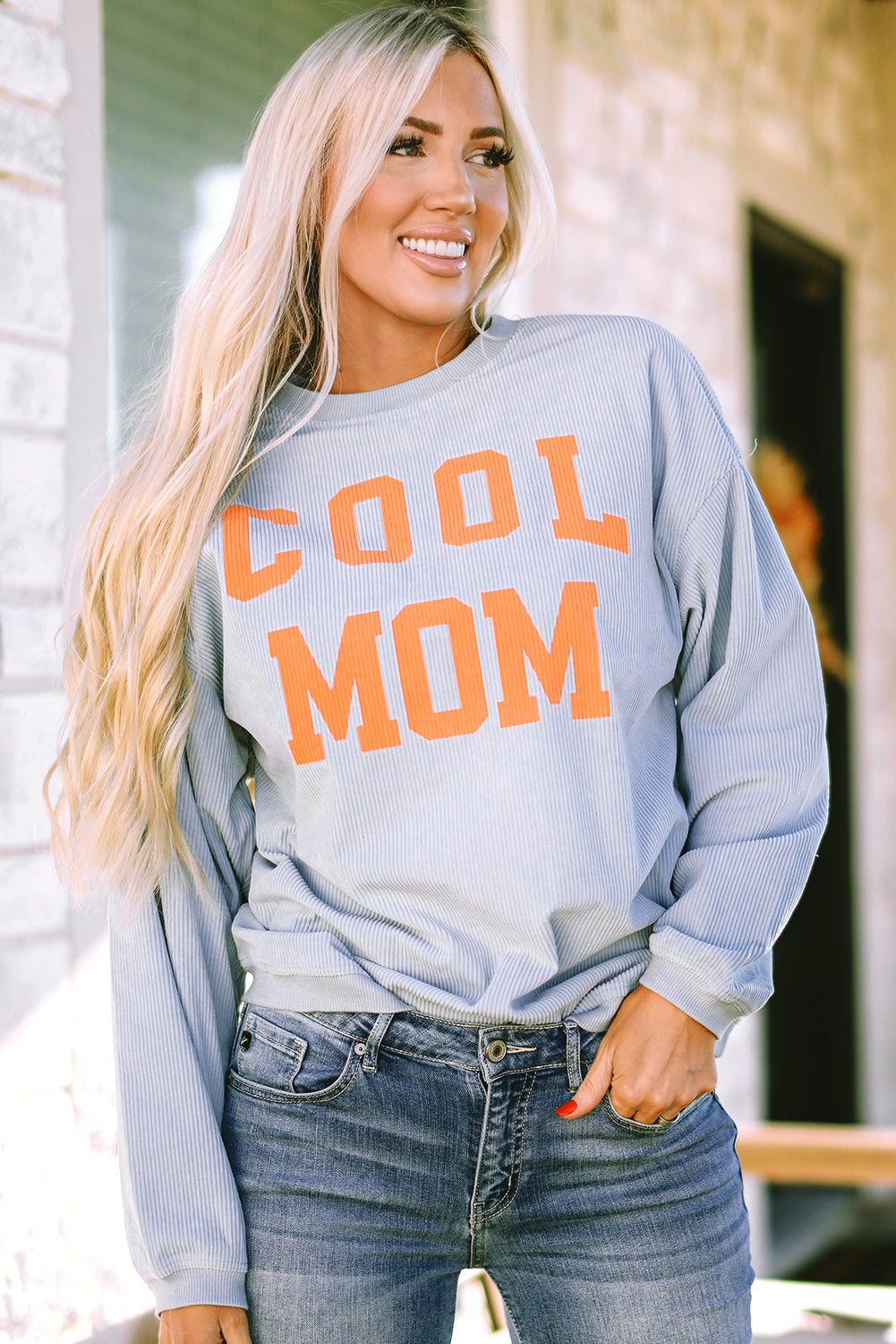 A person with long blonde hair stands facing away, wearing a Gray Cool Mom Graphic Print Cording Sweatshirt and blue jeans.