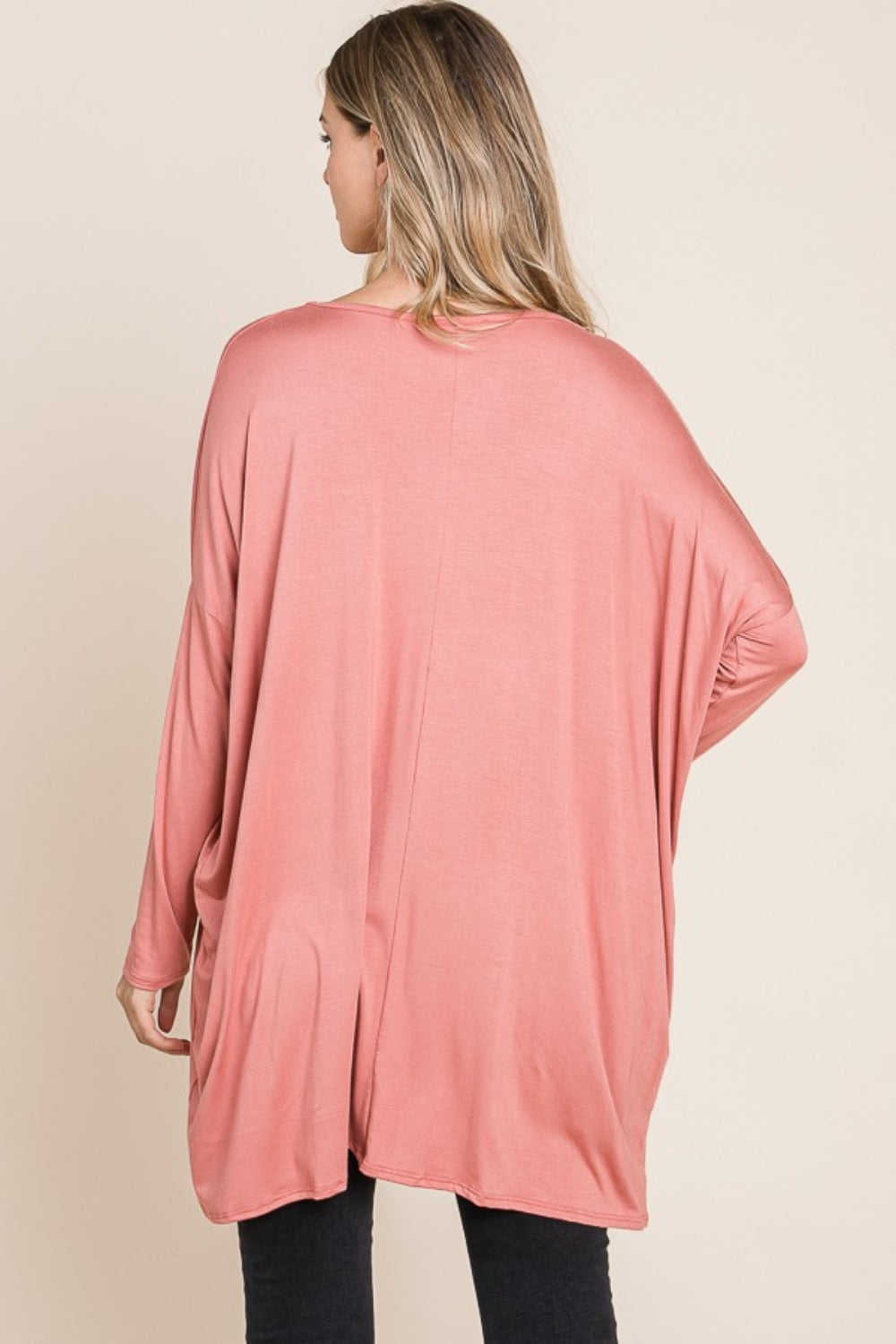 Person in a pink BOMBOM Round Neck Long Sleeve Oversized Top, wearing a long necklace, standing against a neutral background, and posing with one hand touching their hair. This oversized top is made from comfortable fabric that adds to the relaxed vibe.