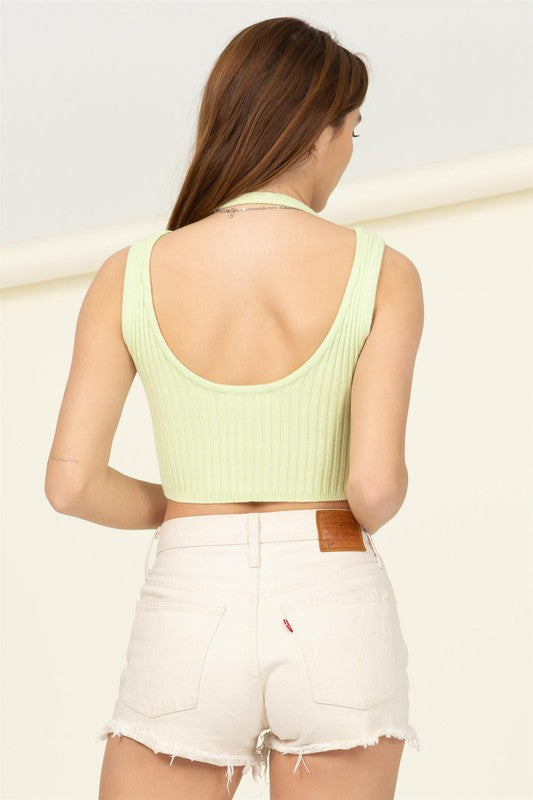 A person with long brown hair smiles while wearing the Perfect Girl Ribbed Open-Back Crop Top in light green, complemented by a delicate necklace.