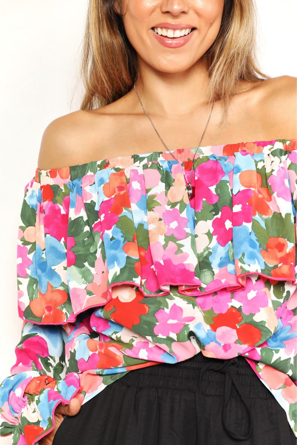 A person wearing a Floral Off-Shoulder Flounce Sleeve Layered Blouse and black pants stands in front of a plain white background.