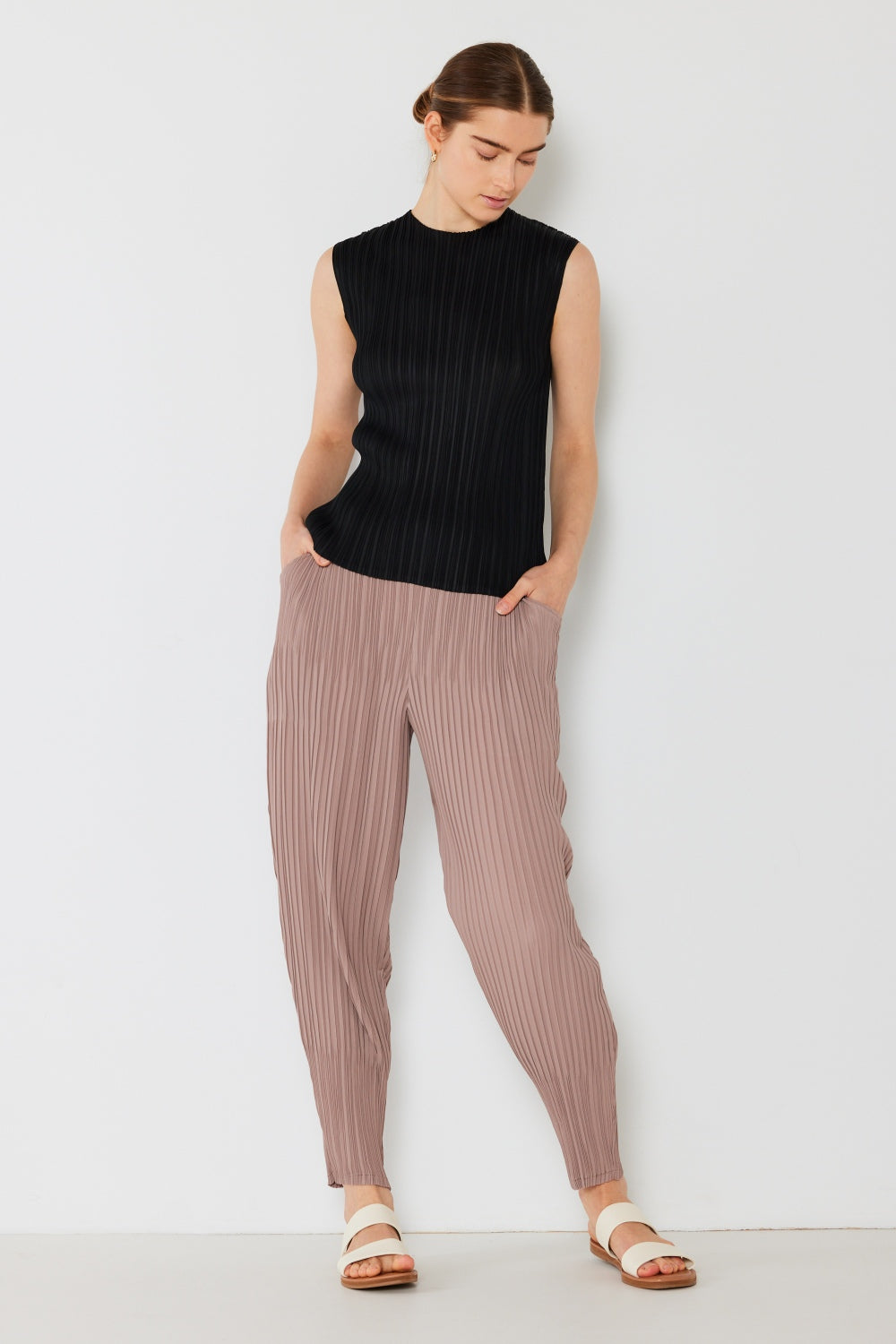 Person wearing a black sleeveless top, Marina West Swim pleated relaxed-fit mauve joggers with a slight drop crotch, and white sandals, standing against a plain white background.