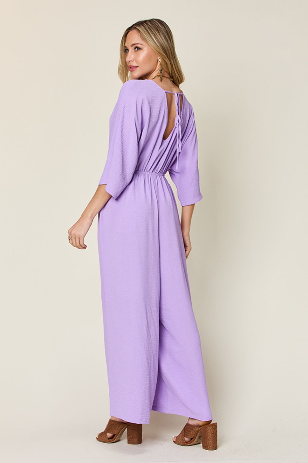 Person wearing the Double Take Full Size Surplice Wide Leg Jumpsuit with Pockets in royal blue, featuring wide legs, a deep V-neckline, and ruched detailing, posing with hands on hips against a plain light-colored background.