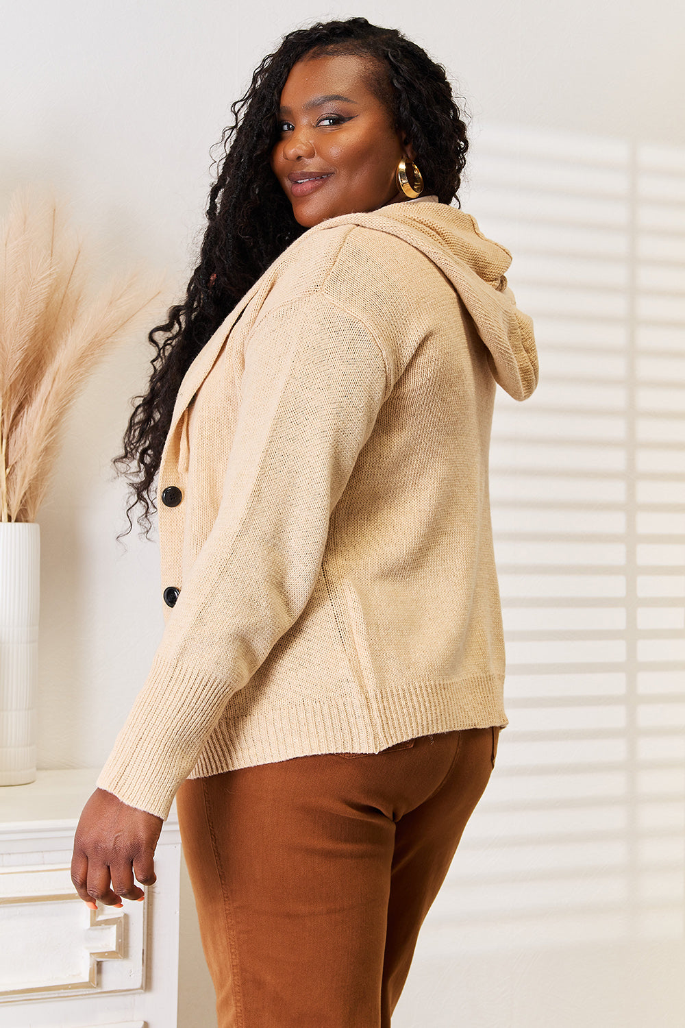 A person stands in a well-lit room wearing the Woven Right Button-Down Long Sleeve Hooded Sweater in a cream color over a white top and brown pants. The individual smiles slightly and poses with one hand in a pocket, against a light background.