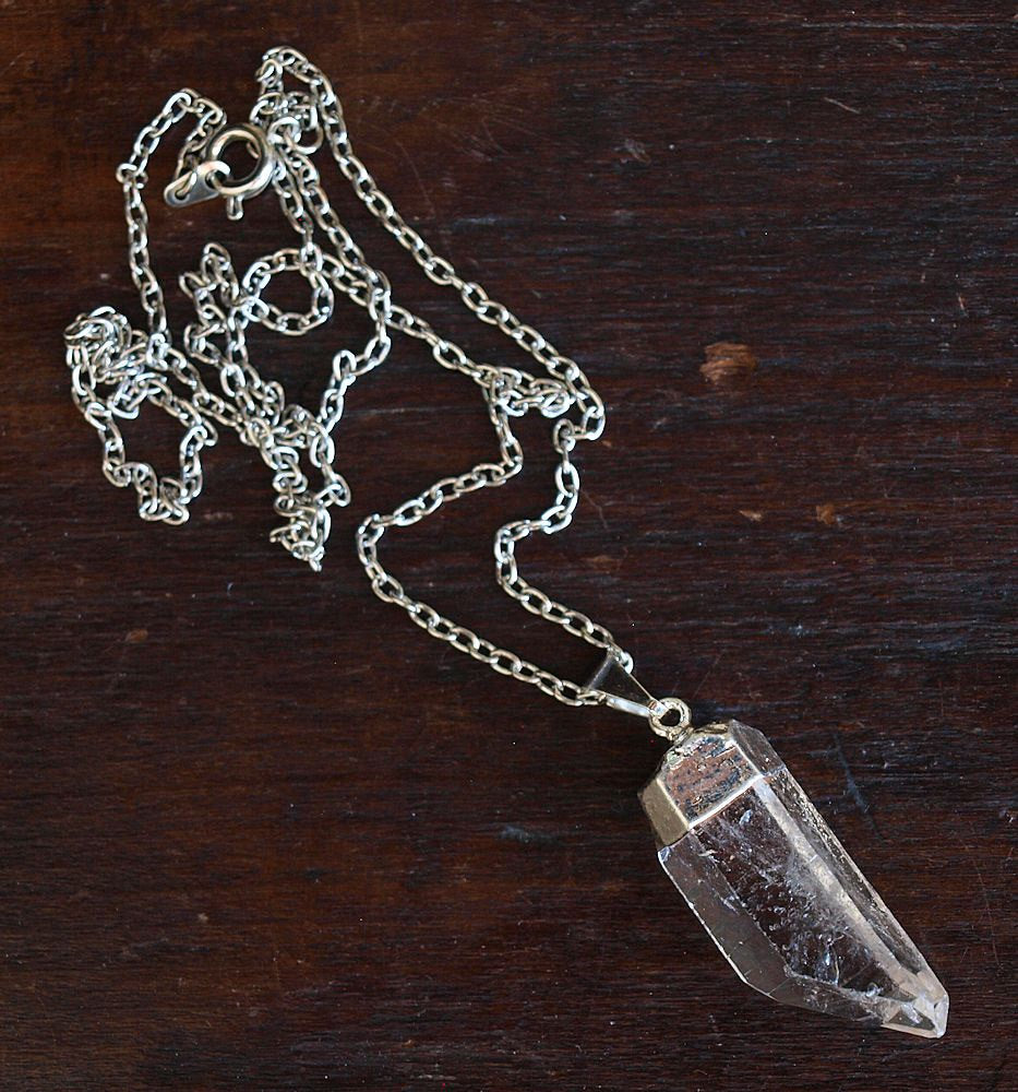 The Raw Quartz Crystal Statement Necklace, adorned with a natural quartz pendant, rests elegantly on a dark wooden surface, symbolizing spiritual growth through its silver chain and clear design.