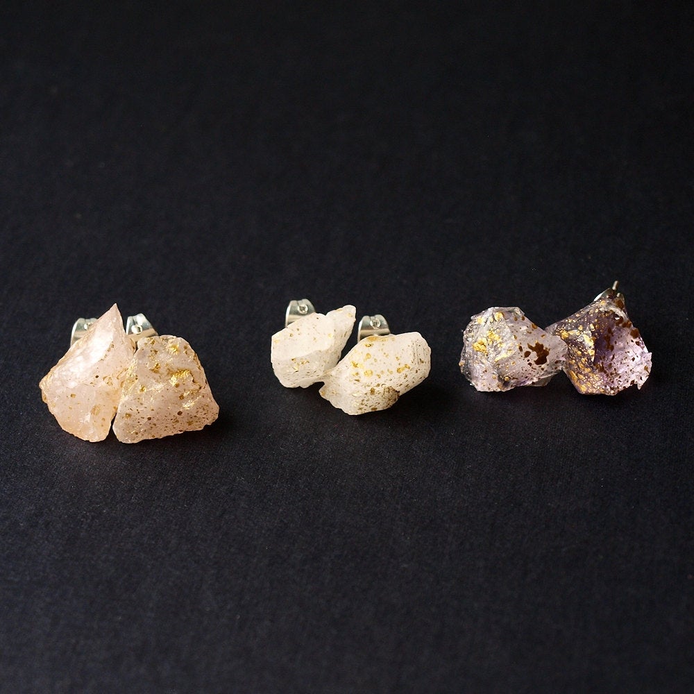 A pair of Gold Splatter & Raw Rose Quartz Chunk Earrings, featuring unpolished stones on silver posts, elegantly displayed on a dark surface.