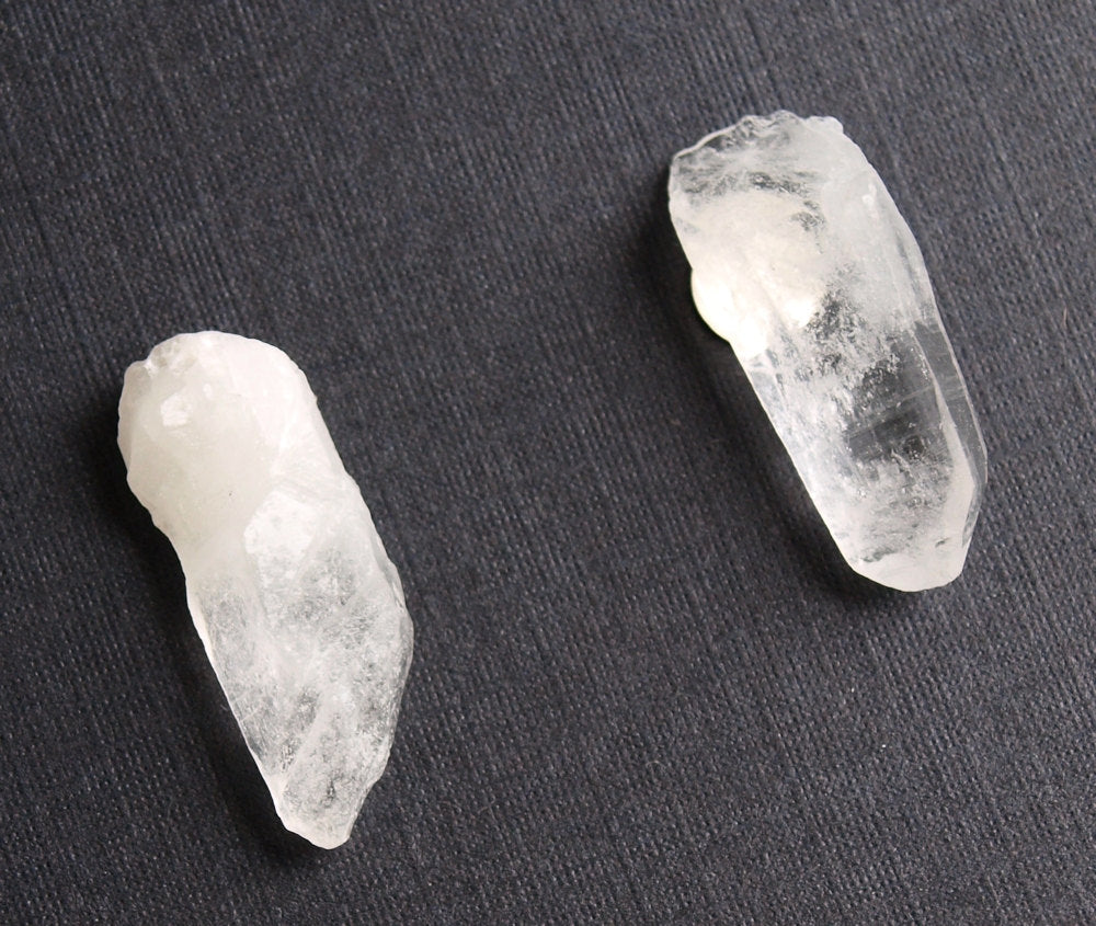 These Raw Quartz Point Earrings beautifully showcase two clear crystal studs with silver backings, artfully set against a dark surface. Ideal for those in pursuit of both style and spiritual development.