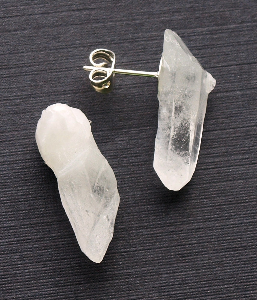 These Raw Quartz Point Earrings beautifully showcase two clear crystal studs with silver backings, artfully set against a dark surface. Ideal for those in pursuit of both style and spiritual development.