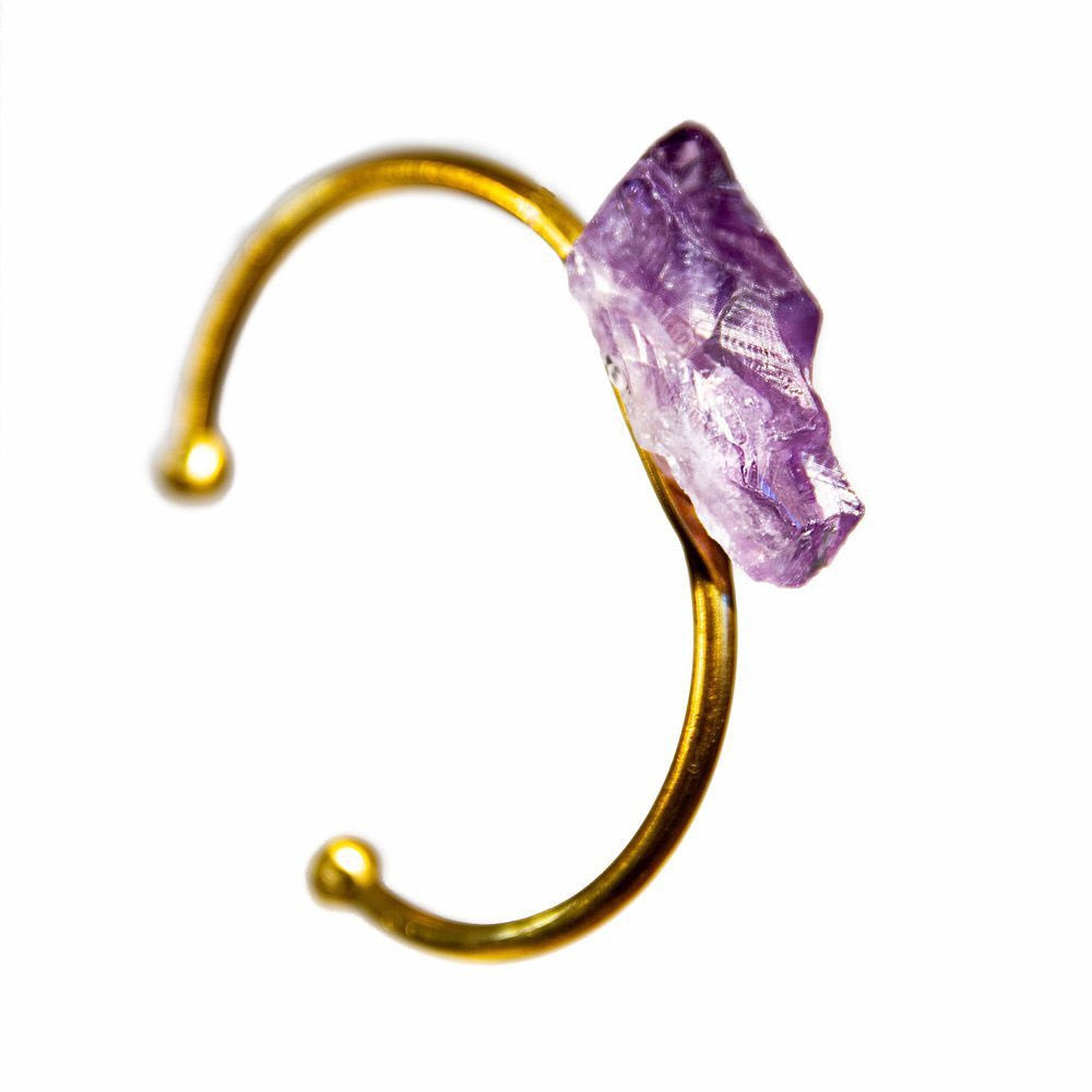 Close-up of a person's wrist wearing the Raw Amethyst Bangle, an adjustable bracelet with a large, rough purple stone set on a gleaming gold band.