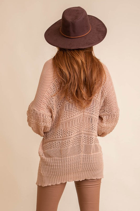 A person with long hair, wearing an oversized Knit Netted Cardigan, a crop top, and denim shorts, stands in a light-colored room.