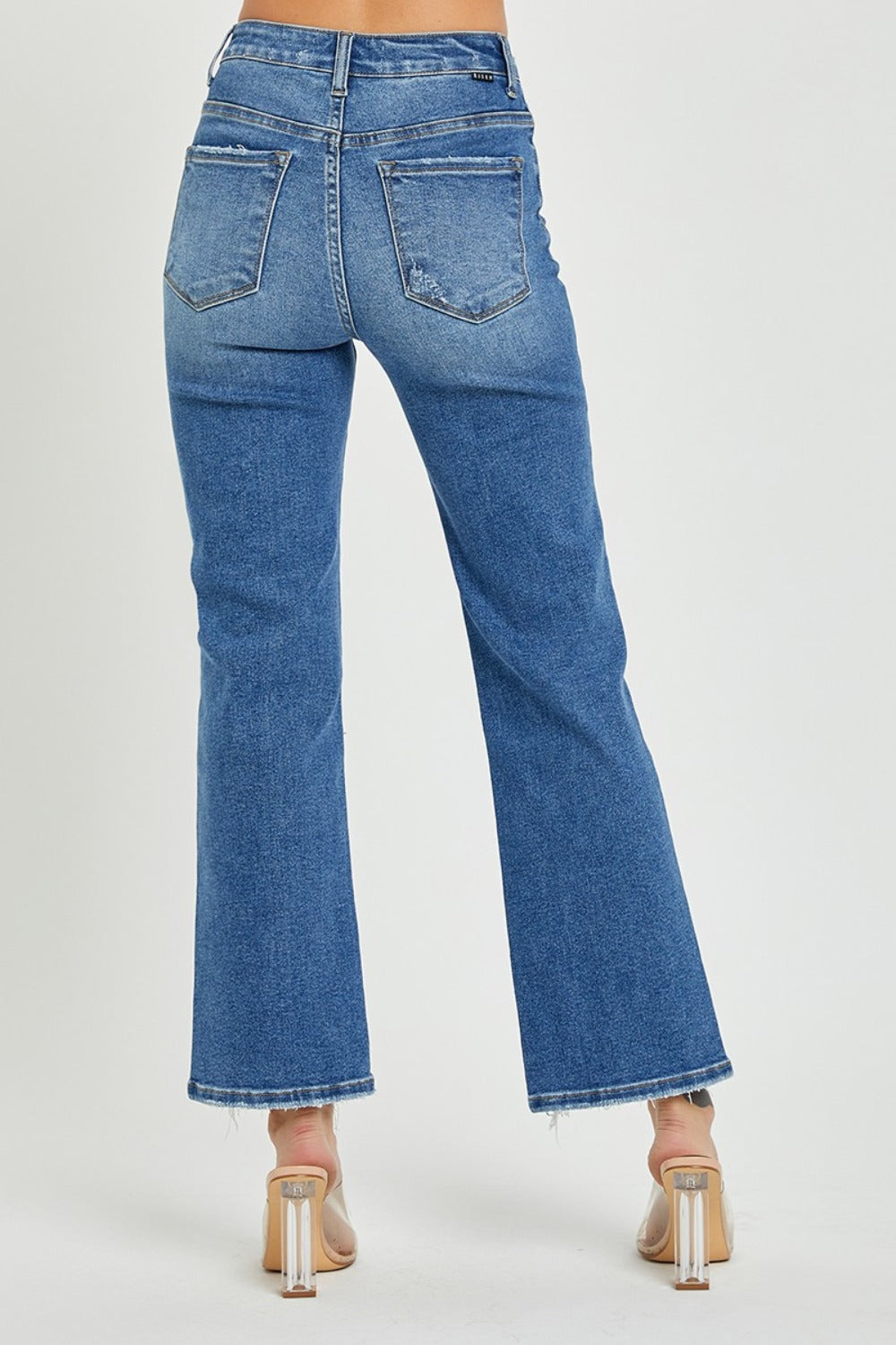 Person wearing RISEN High Rise Straight Jeans with frayed hem and clear-strap heels, standing against a plain background, showcasing a classic silhouette.