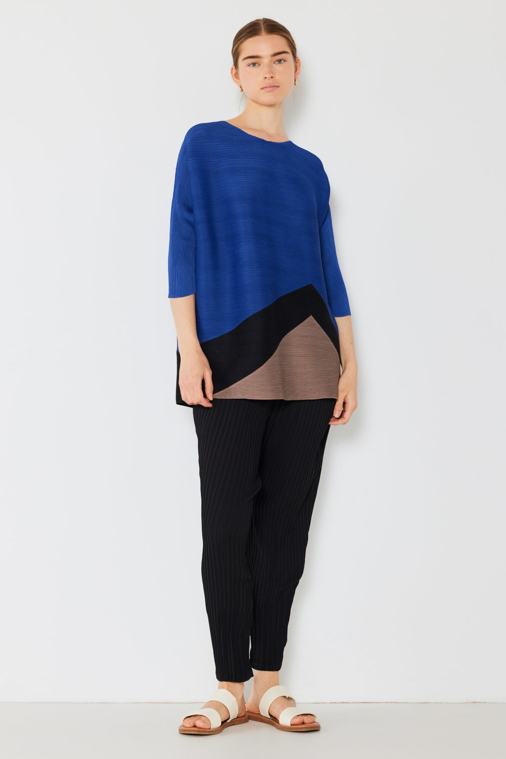 A person wearing a loose-fitting, trendy and eye-catching Marina West Swim Pleated Horizontal Rib Color Block Top, paired with black pinstriped pants.