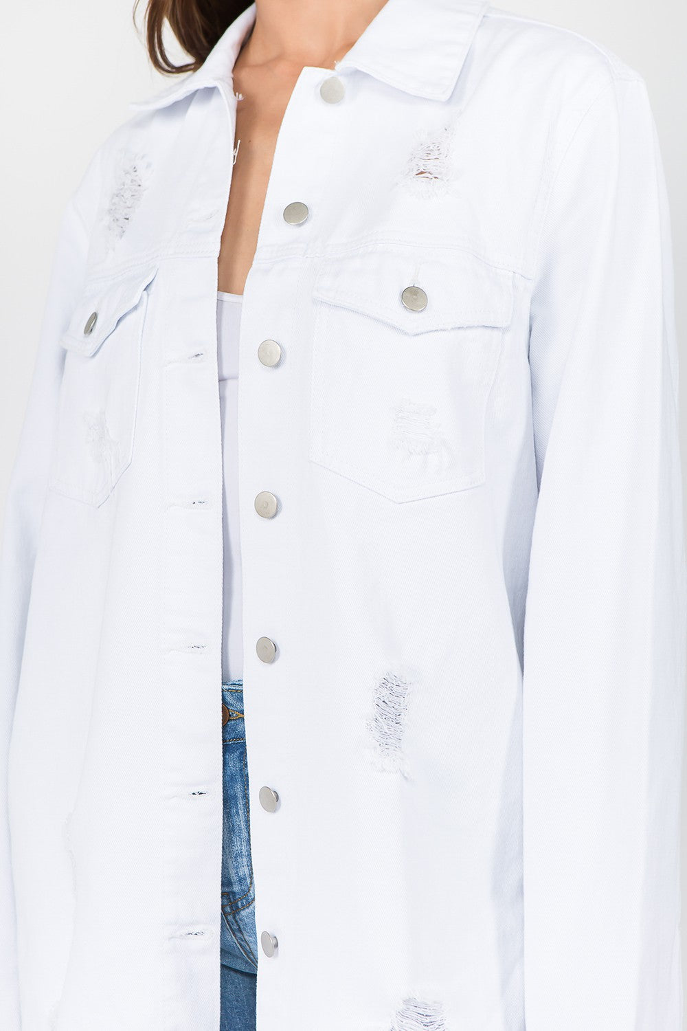 A woman stands against a plain background wearing an American Bazi Distressed Frayed Hem Denim Jacket styled in a vintage manner and paired with distressed denim shorts featuring a frayed hem.