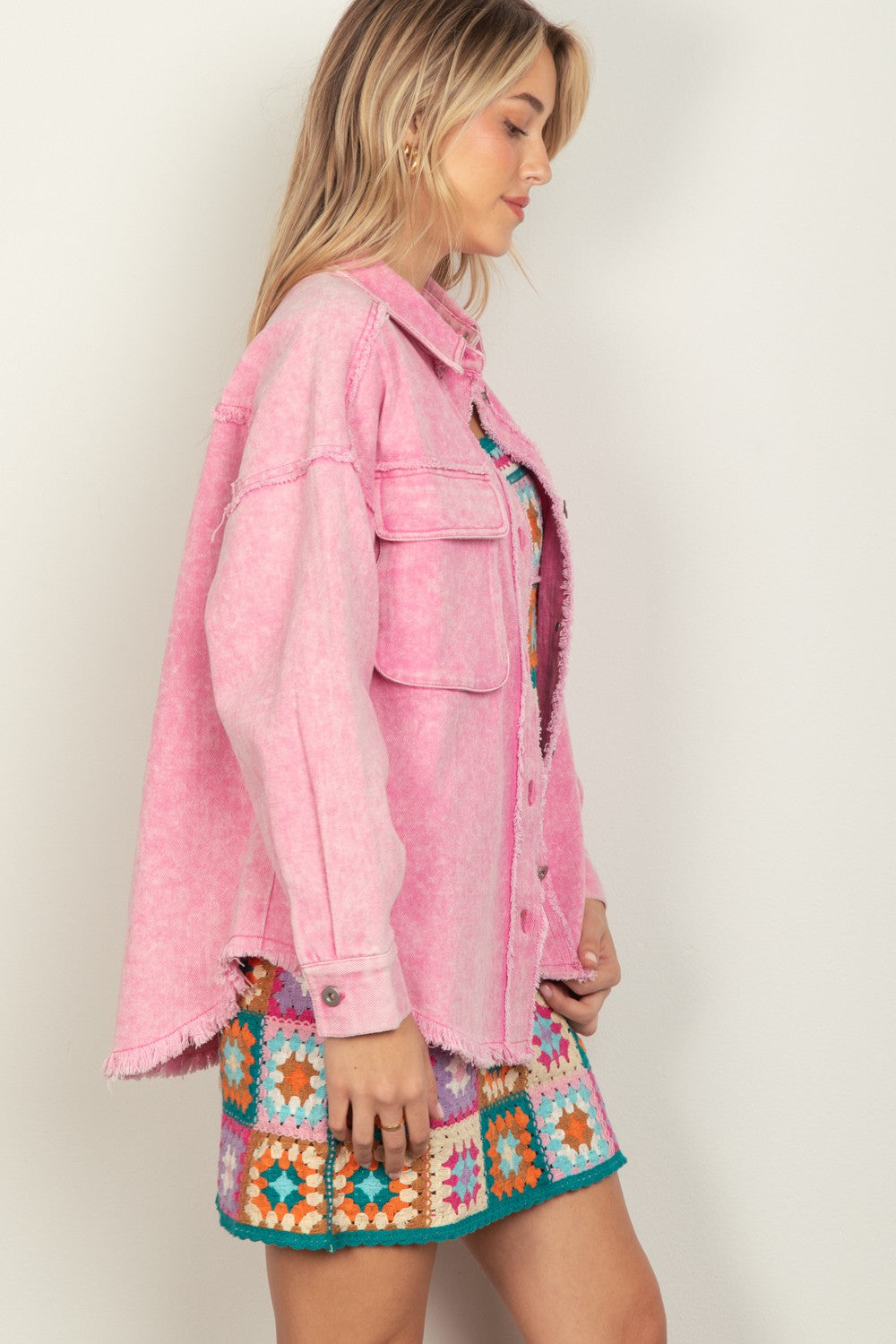 Person wearing a VERY J Full Size Button Up Raw Hem Long Sleeve Jacket in pink over a colorful, patterned dress, standing against a plain background.