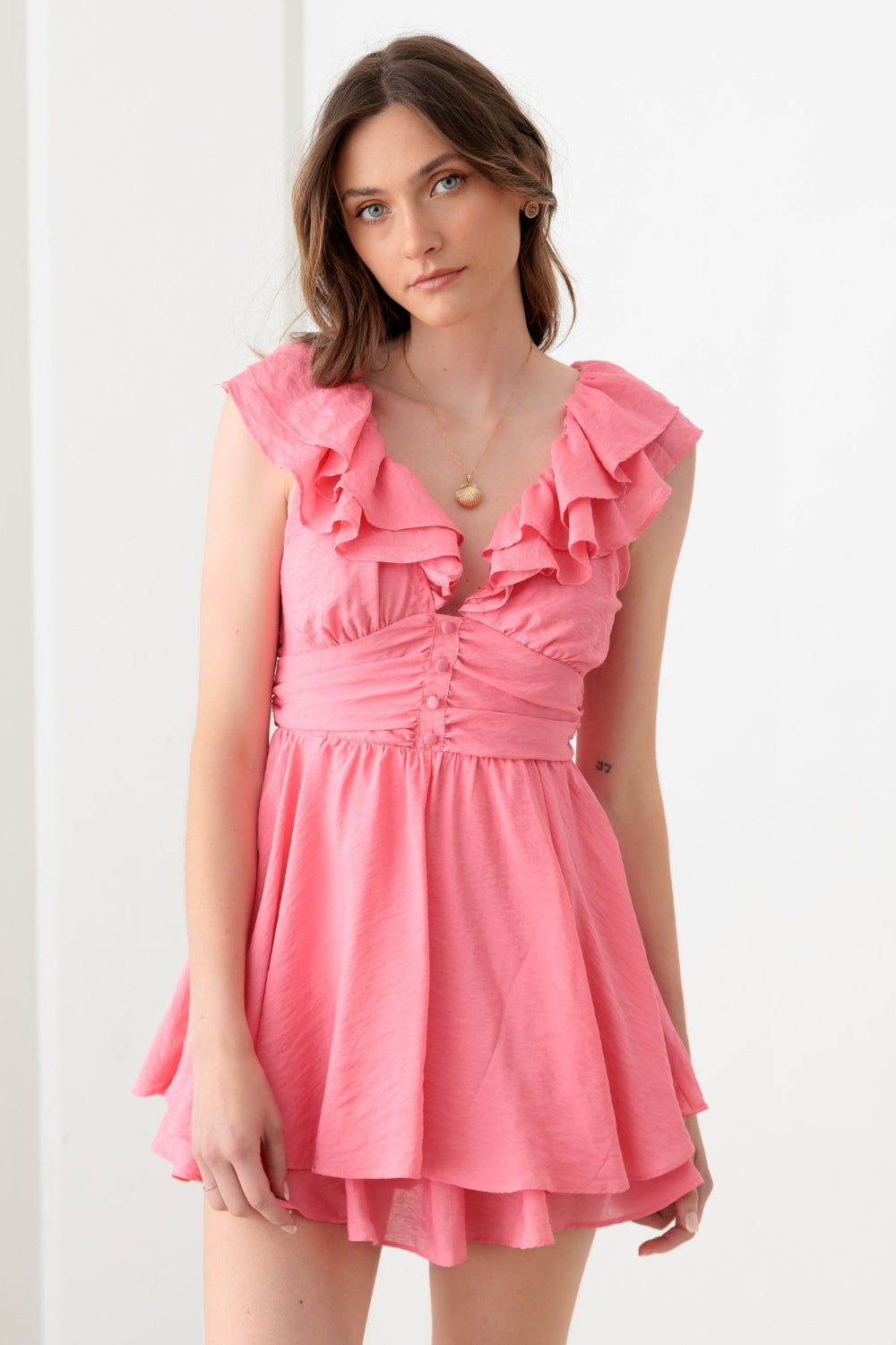 A person wearing a Mustard Seed Tie Back Front Button Ruffled Romper, ideal for a boho-inspired summer wardrobe, stands in front of a plain white background.