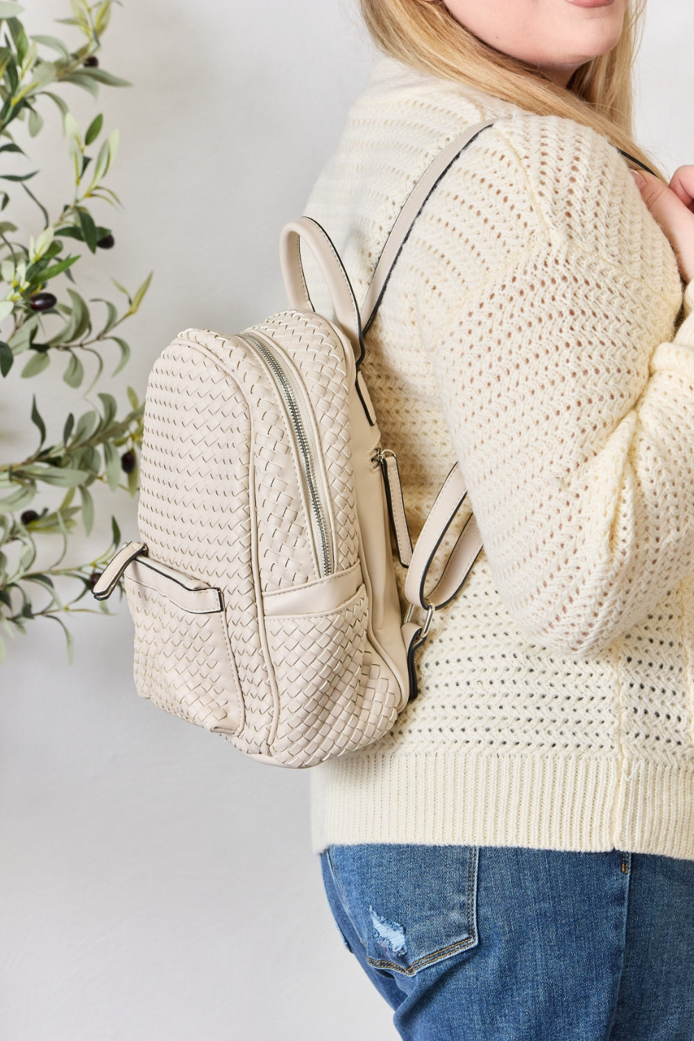 A person wearing a cream sweater and jeans is carrying the SHOMICO PU Leather Woven Backpack in brown.