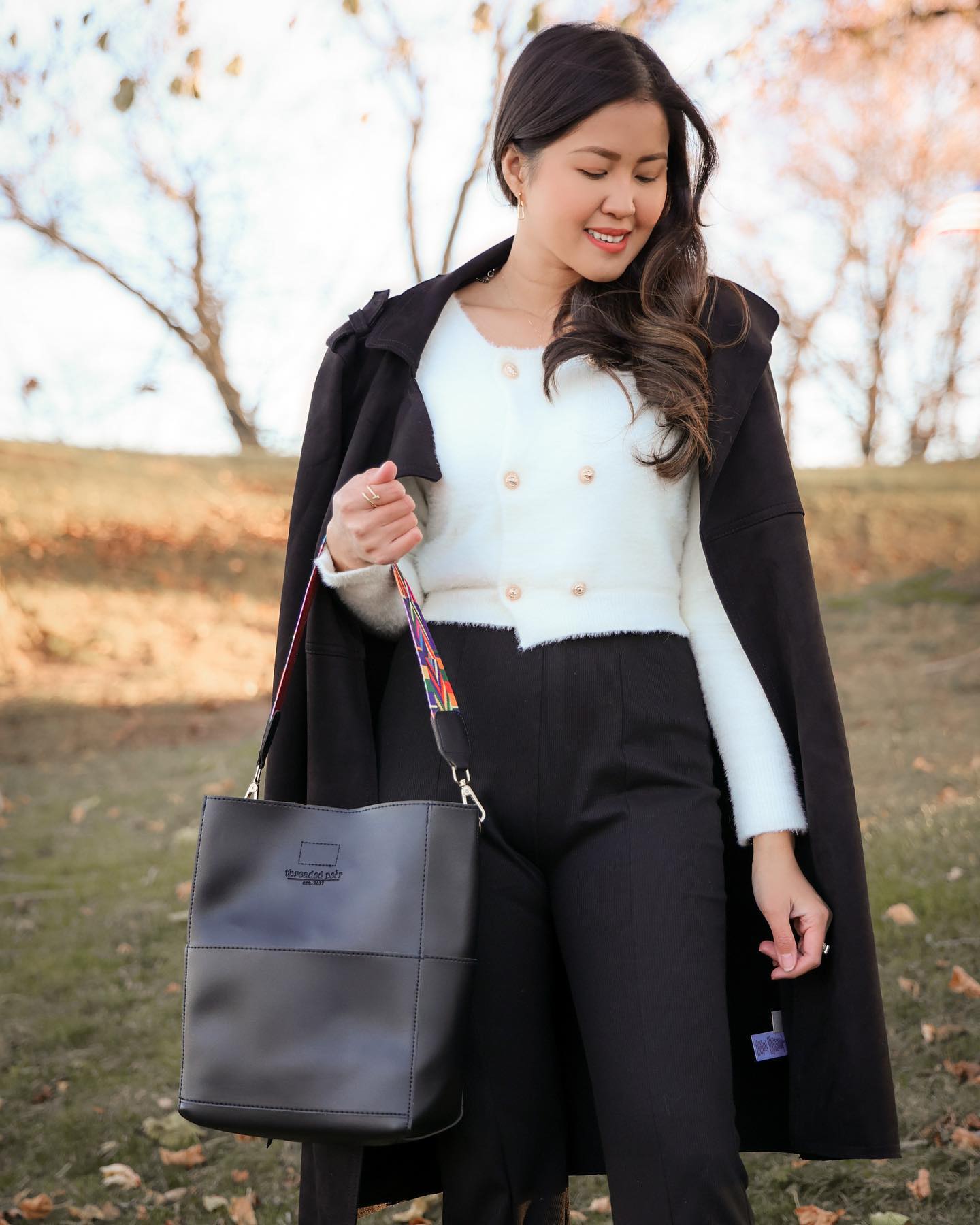 A woman sits on a bench, placing a Threaded Pear wristlet into her large Jordyn Handbag.