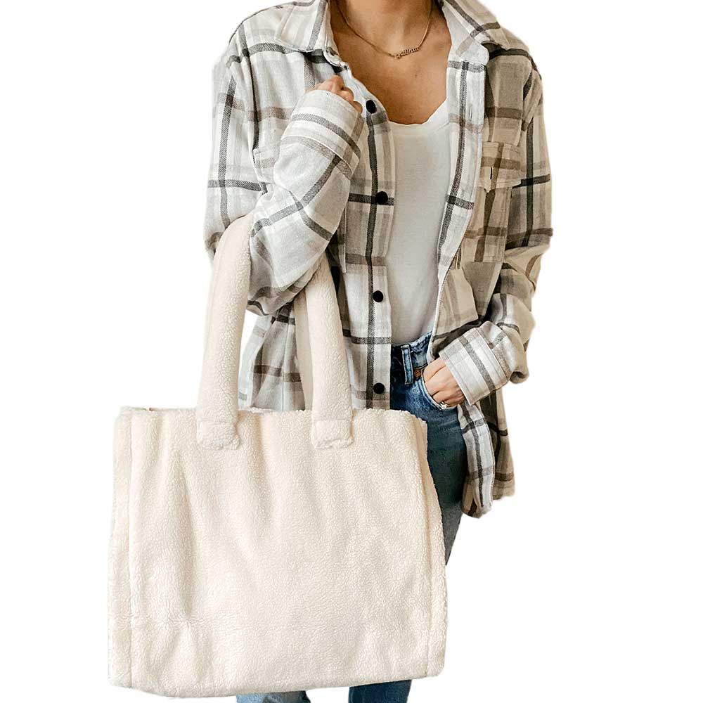 The Astrid Shopper Tote is a tote bag made from cozy blue teddy fleece. It showcases a straightforward rectangular shape with two sturdy handles and comes equipped with a zippered interior pocket for extra functionality.