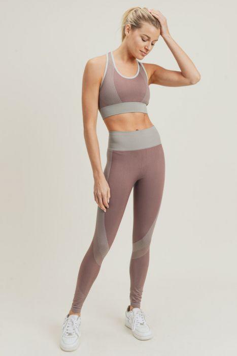 A person wearing a mauve and grey athletic outfit, including a sports bra and Chevron Track Seamless Highwaist Leggings with tummy control, and white sneakers, standing against a plain backdrop.