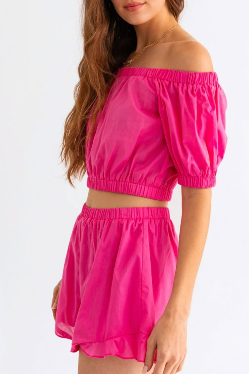 Person wearing the Le Lis Off Shoulder Crop Top and Ruffled Shorts Set, featuring a bright pink, off-the-shoulder crop top with puffed sleeves paired with matching high-waisted ruffled shorts, the perfect summer outfit.