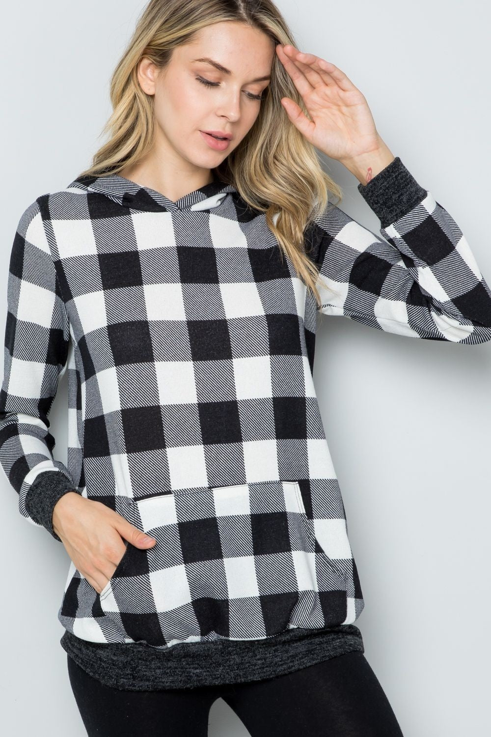 A woman wearing the Celeste Full Size Contrast Plaid Long Sleeve Hoodie smiles while standing against a plain background, showcasing her casual wardrobe.