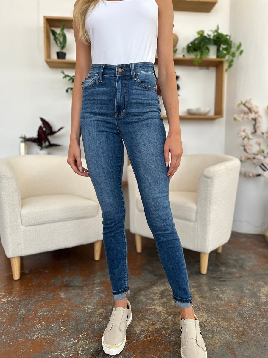 Person wearing Judy Blue Full Size Cuffed Hem Skinny Jeans and a white T-shirt, posing with one hand in pocket and feet in black open-toe shoes.