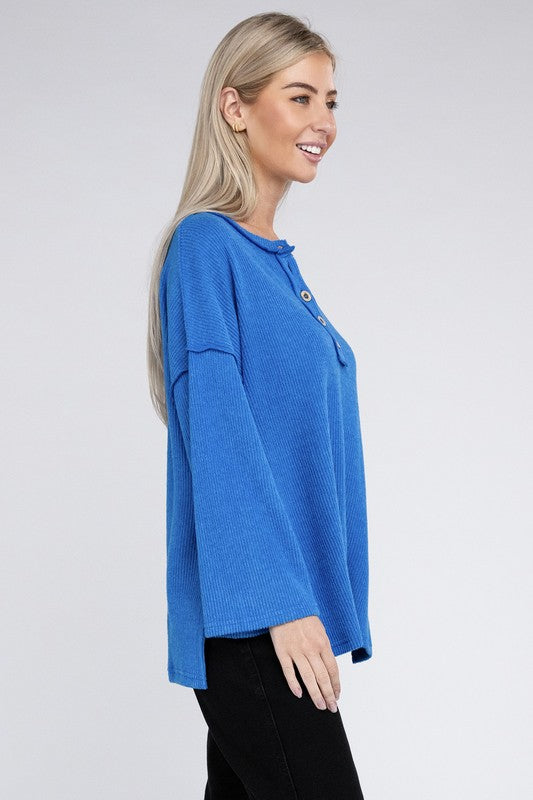 Woman in a blue Ribbed Brushed Melange Hacci Henley sweater with button details posing with her hand on her chin.