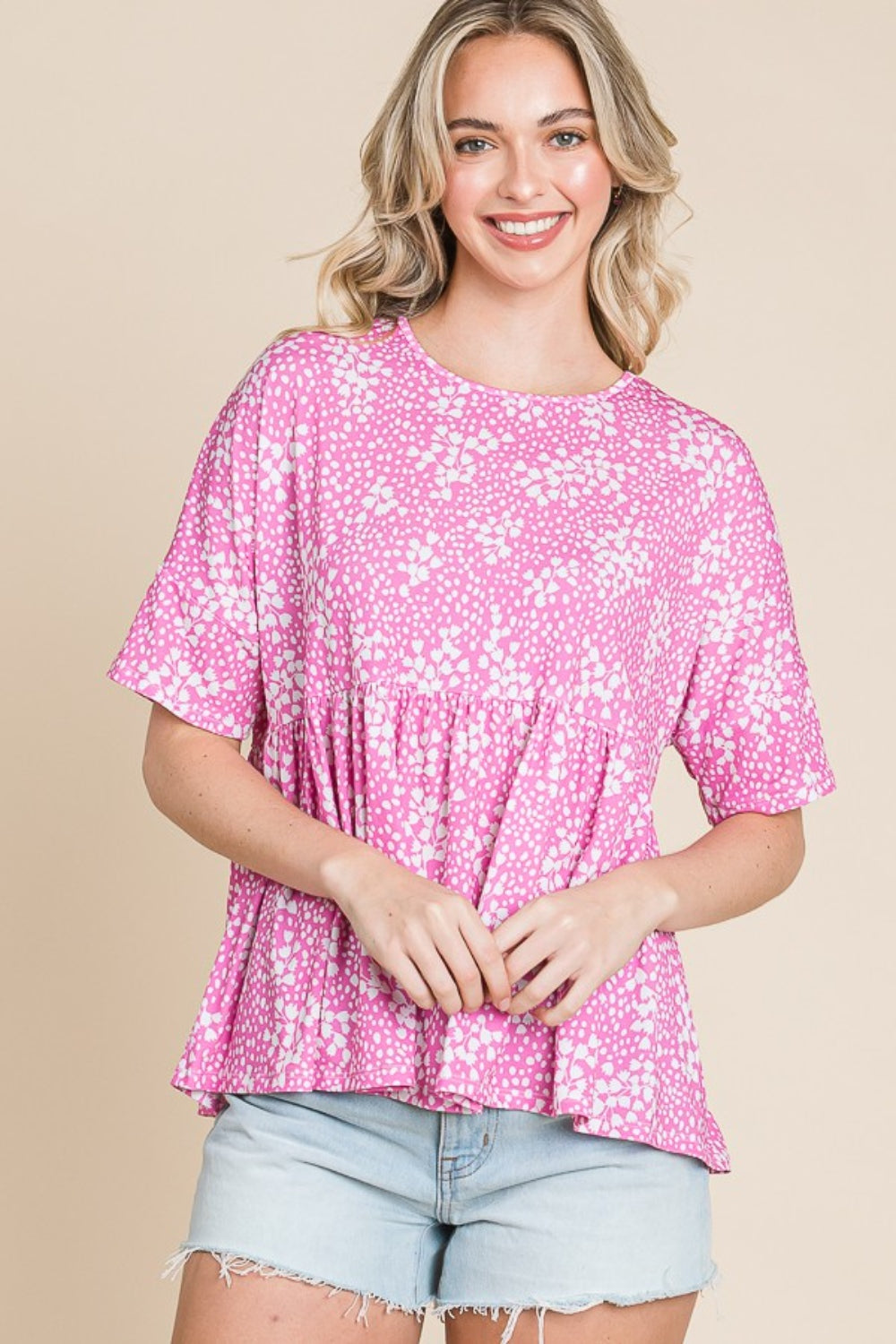 A person wearing a BOMBOM Floral Round Neck Peplum Blouse and denim shorts stands smiling against a beige background.