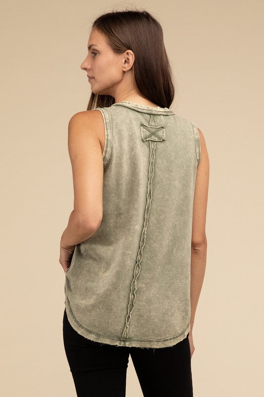 A woman with long brown hair is wearing the Washed Half-Button Raw Edge Sleeveless Henley Top in green and black pants, standing against a beige background.