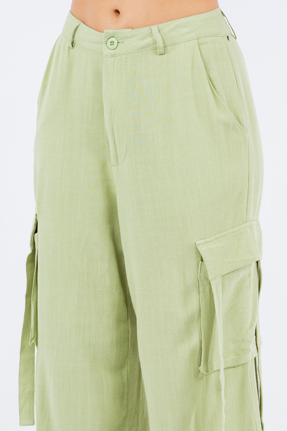 A person is wearing American Bazi light green linen wide leg cargo pants with multiple pockets and white sneakers.