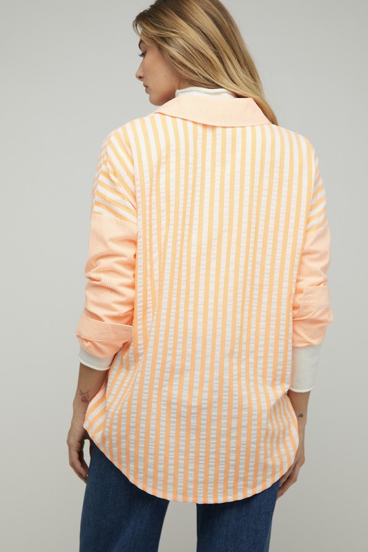 A person wearing a light pink Stripe Button Down Long Sleeve Shirt with rolled-up sleeves and jeans stands with their hands behind their head against a plain background.