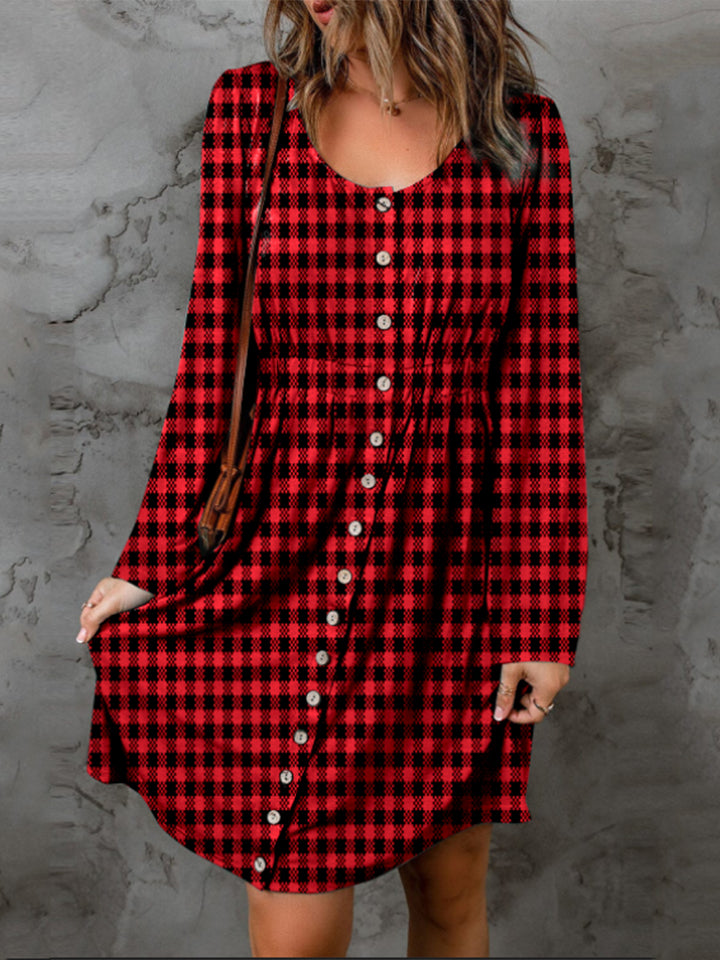 A person wearing the Double Take Full Size Plaid Round Neck Long Sleeve Magic Dress stands against a textured gray wall.