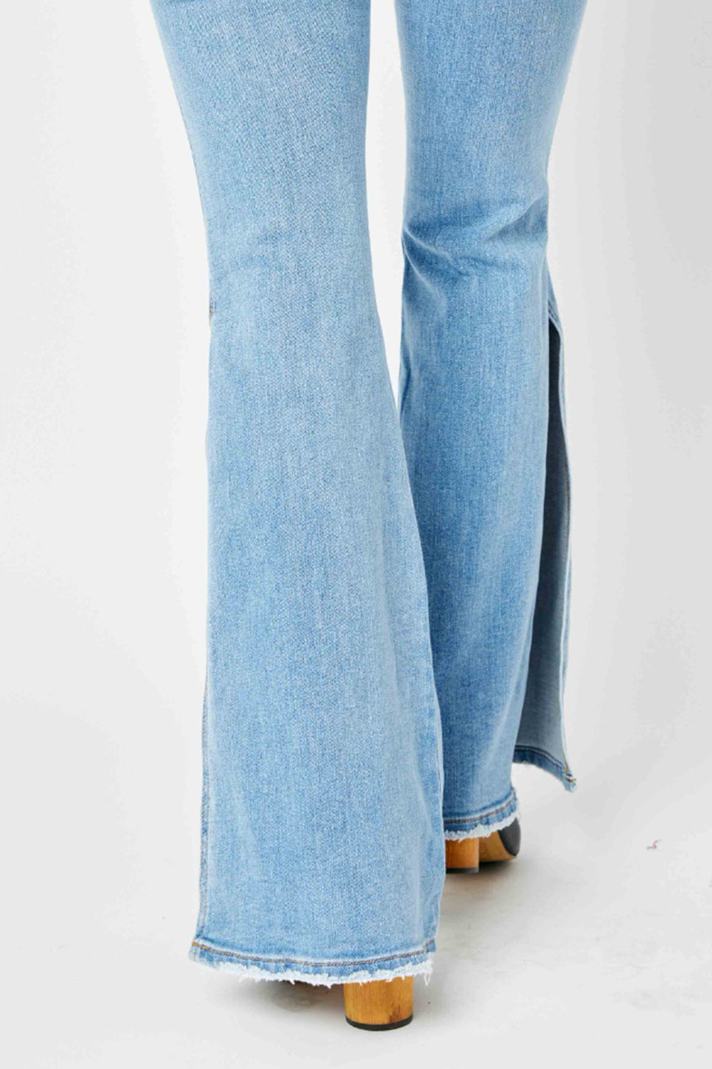 A person is wearing Judy Blue Full Size Mid Rise Raw Hem Slit Flare Jeans with a flattering silhouette and black open-toe shoes.