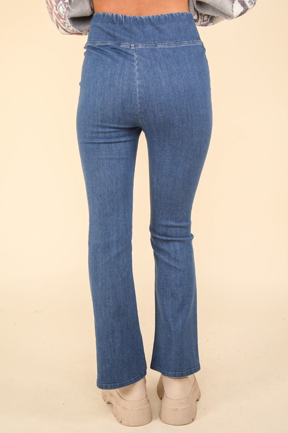 Person wearing VERY J Washed Denim Stretchy Crossover Waist Leggings with a hint of flared leg, and beige ankle-length boots. Only the lower half of the body is visible.