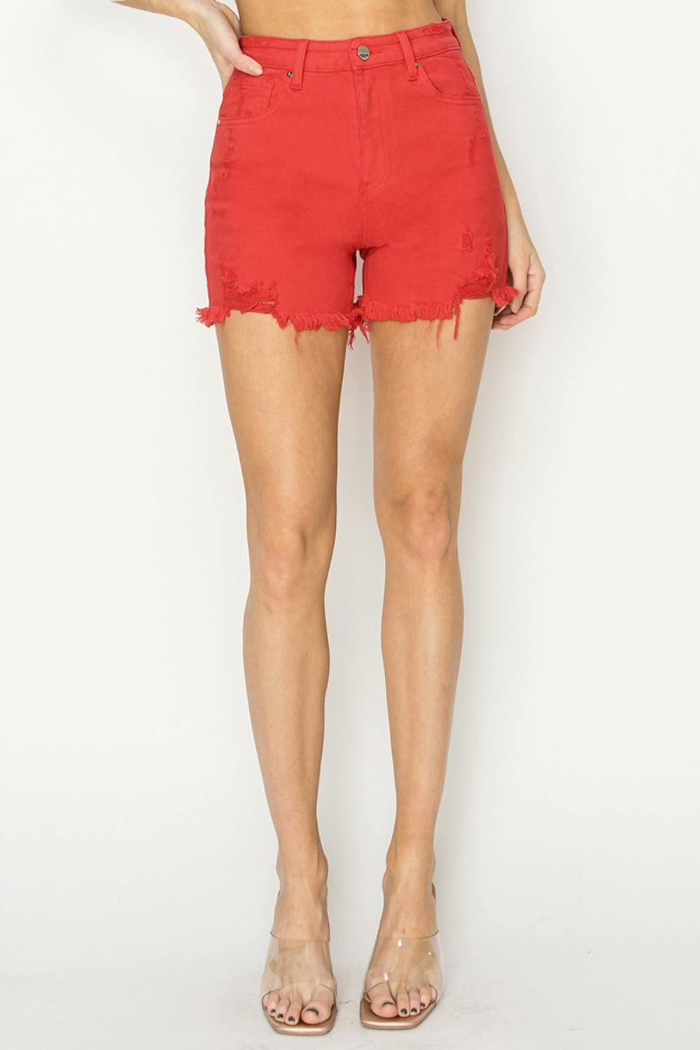 Close-up of a person wearing trendy RISEN High Rise Distressed Denim Shorts with distressed hems and pockets. The versatile wardrobe essential shorts feature a button and zip closure.