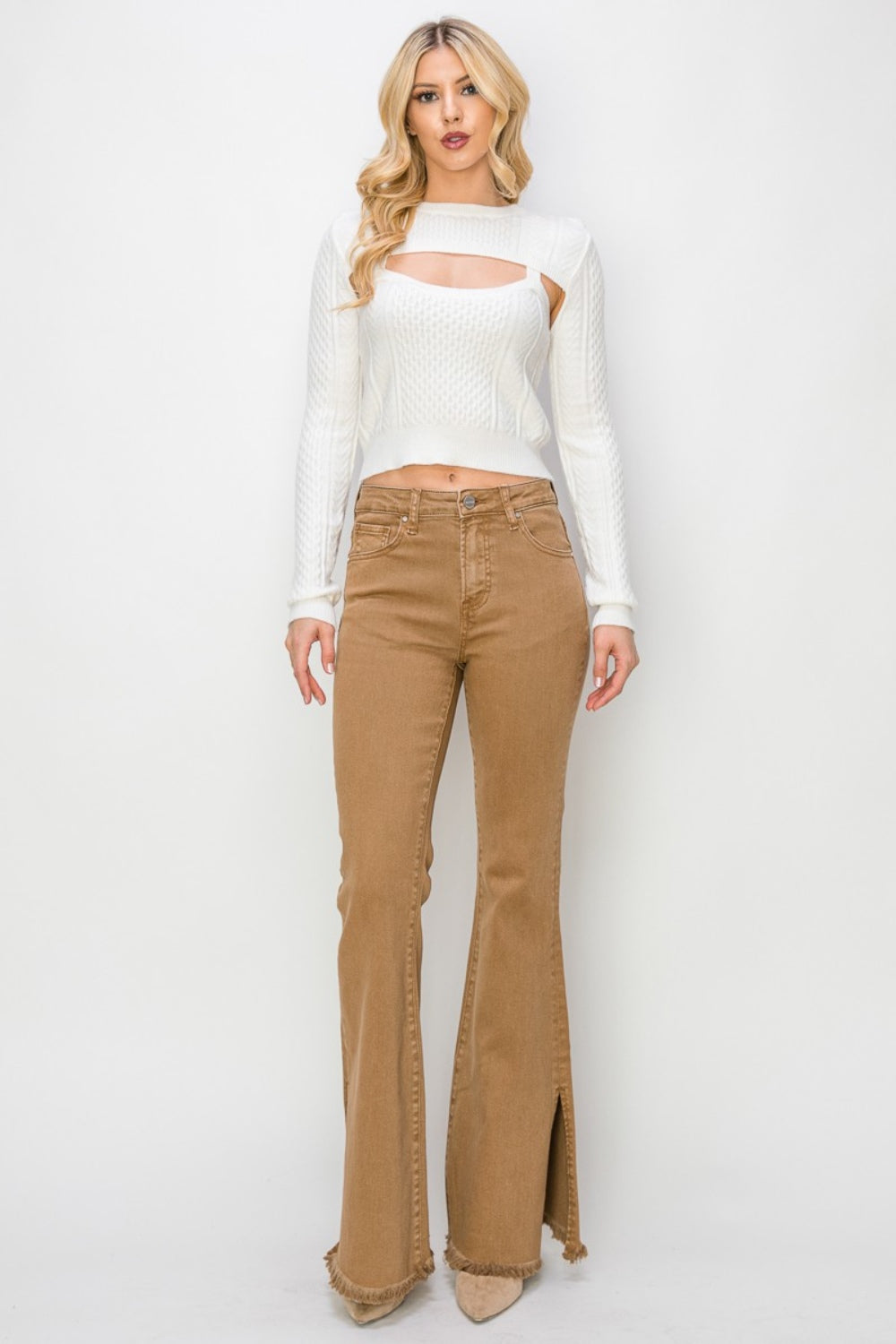 Wearing the RISEN Bailey Full Size High Waist Side Slit Flare Jeans with frayed hems, a person pairs them with beige boots against a white background.