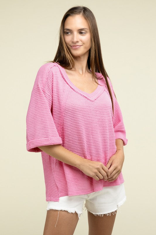 A person is dressed in a Brushed Waffle Exposed-Seam 3/4 Sleeve Top and white shorts, perfect for a casual wardrobe. They stand against a plain background, effortlessly embodying relaxed style.